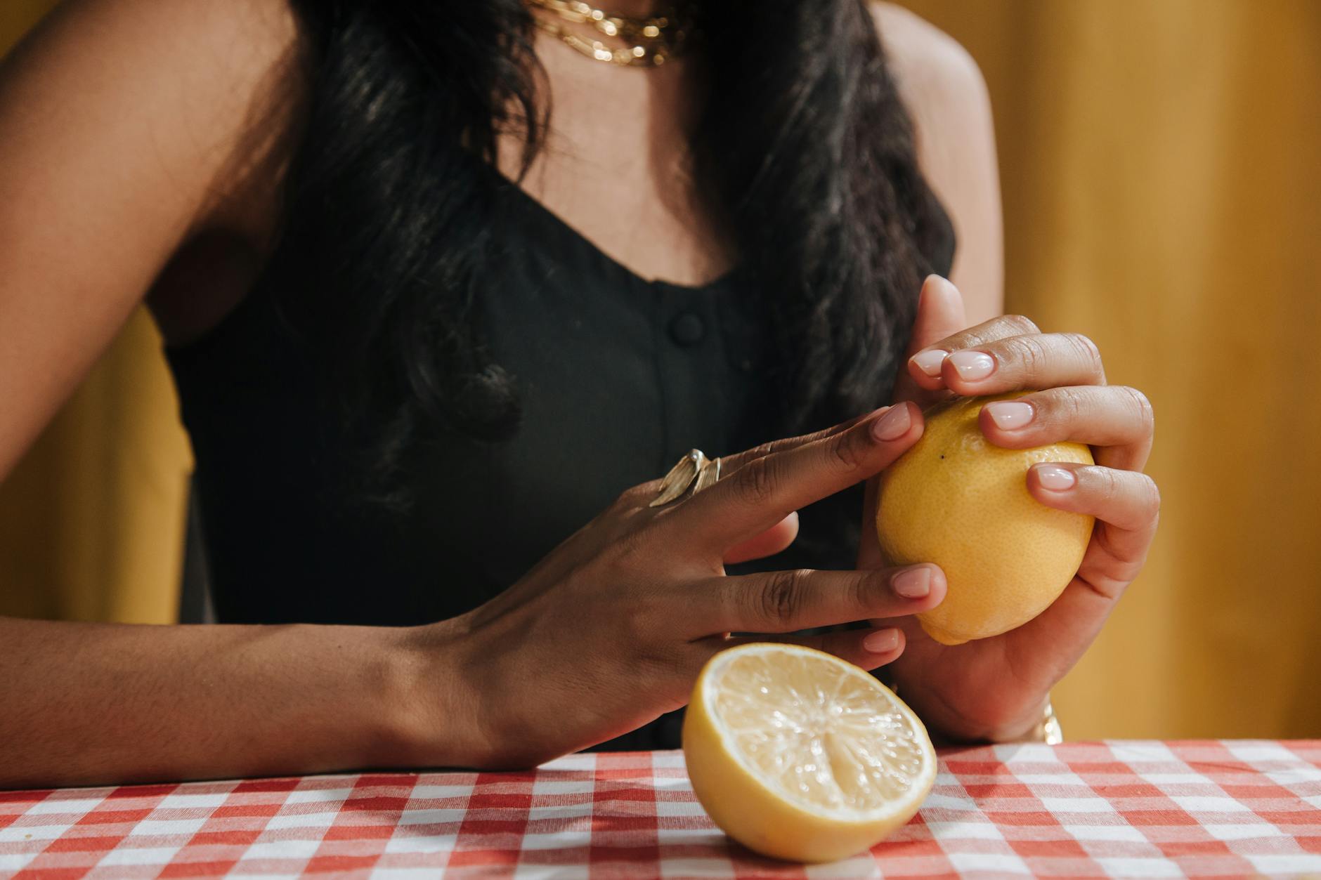 Hand with white nails holding a fresh lemon on a soft pink background surrounded by lemons