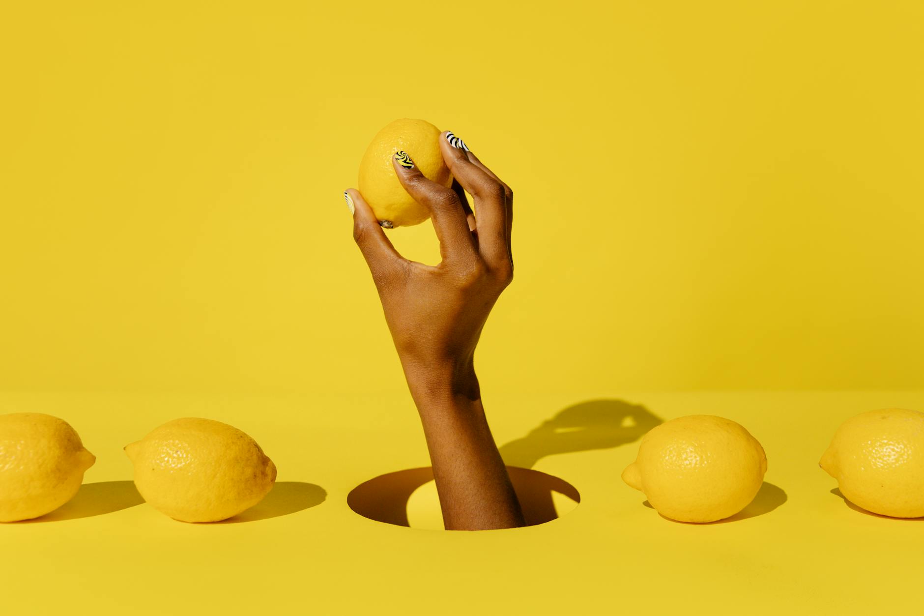 A hand holding a fresh lemon against a bright yellow background, symbolizing fresh sensation and citrus-inspired design