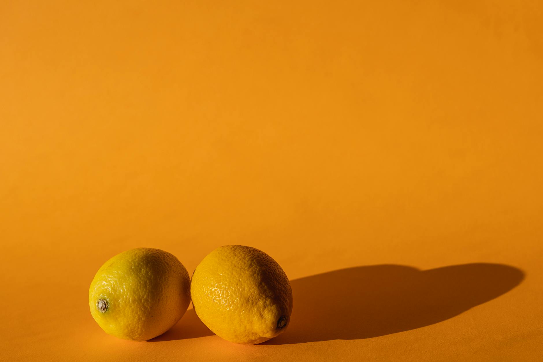 Hand holding a lemon clitoral vibrator against a bright yellow background